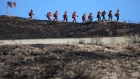 CANYON COUNTRY, CALIFORNIA - OCTOBER 25: Inmate firefighters march past an American flag, while led by a fire captain, as they work to put out hot spots from the Tick Fire on October 25, 2019 in Canyon Country, California. The fire has blackened 4,300 acres thus far with around 40,000 people under mandatory evacuation orders. The inmates are from one of the 44 state prison fire camps, where inmates perform firefighting duties during the wildland fire season, for credit for early release and minimal pay. (Photo by Mario Tama/Getty Images)