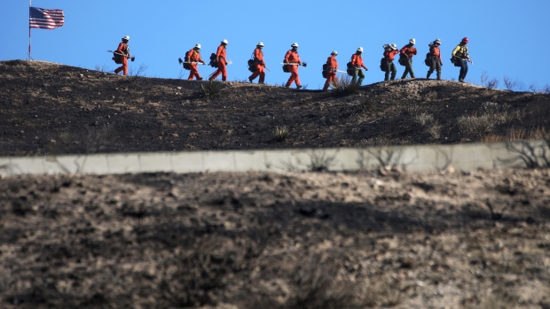 CANYON COUNTRY, CALIFORNIA - OCTOBER 25: Inmate firefighters march past an American flag, while led by a fire captain, as they work to put out hot spots from the Tick Fire on October 25, 2019 in Canyon Country, California. The fire has blackened 4,300 acres thus far with around 40,000 people under mandatory evacuation orders. The inmates are from one of the 44 state prison fire camps, where inmates perform firefighting duties during the wildland fire season, for credit for early release and minimal pay. (Photo by Mario Tama/Getty Images)