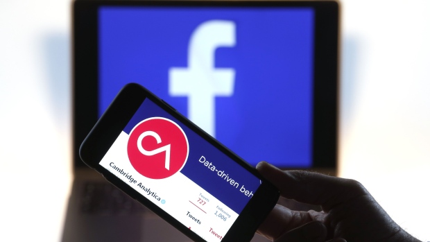 The verified Twitter Inc. page of Cambridge Analytica, displaying their logo and company name, sit on an Apple Inc. iPhone against a backdrop of the Facebook Inc. sign shown on a computer screen in this arranged photograph in London, U.K., on Thursday, March 22, 2018. Facebook Inc.’s co-founder and chief executive officer Mark Zuckerberg has been called to appear before a House panel as fallout continues from revelations that Cambridge Analytica had siphoned data from some 50 million Facebook users as it built a election-consulting company that boasted it could sway voters in contests all over the world. 