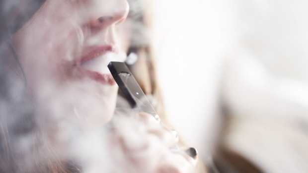 A person smokes a Juul Labs Inc. e-cigarette in this arranged photograph taken in the Brooklyn Borough of New York, U.S., on Sunday July 8, 2018. Juul Labs, the maker of the popular e-cigarette brand that has recently come under fire from health officials over its popularity with young adults, plans to introduce a line of lower-nicotine pods. The company will begin to sell pods with a 3-percent nicotine concentration in its mint and Virginia tobacco flavors later this year, according to a statement Thursday. 