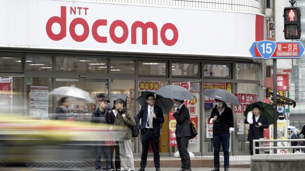 Pedestrians wait to cross a road in front of an NTT Docomo Inc. store in Tokyo, Japan