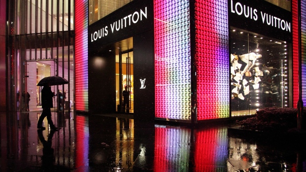 A man holding an umbrella walks past a Louis Vuitton store, operated by LVMH Moet Hennessy Louis Vuitton SA, in Shanghai, China. 