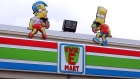 Milhouse Van Houten and Bart Simpson props sit atop a Simpsons-styled "Kwik-E-Mart" 7-Eleven store