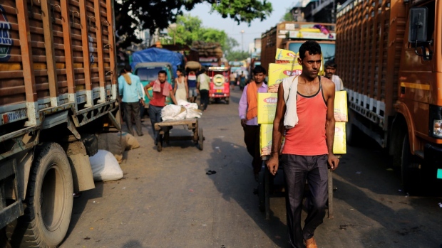 A worker pulls a cart past trucks at a wholesale market in Delhi, India, on Sunday, July 7, 2019. India's new Finance Minister Nirmala Sitharaman resisted calls for a fiscal boost to spur a weakening economy, sticking instead to a plan to narrow the budget deficit over time by keeping spending in check. 
