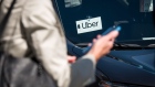 A traveler uses a smartphone in front of a vehicle displaying Uber Technologies Inc. signage at the Oakland International Airport in Oakland, California, U.S., on Tuesday, Aug. 6, 2019. Uber Technologies Inc. is scheduled to release earnings figures on August 8. 