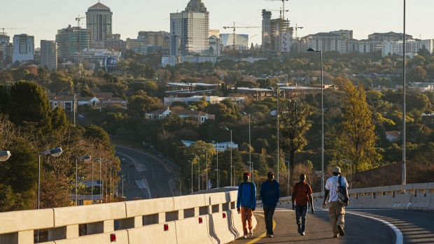 Pedestrians walk along a roadway back-dropped by commercial and residential buildings in the Sandton district of Johannesburg, South Africa. Photographer: Waldo Swiegers/Bloomberg