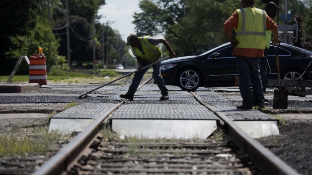 Workers smooth a road transition near a railroad crossing while laying asphalt on a state highway in Streator, Illinois. Photographer: Daniel Acker