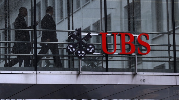 Employees pass between offices as UBS Group AG logo sits on a walkway at the UBS headquarters in Zurich, Switzerland.
