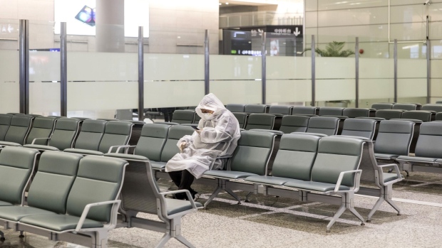 A man wearing a protective mask and raincoat sits in the arrivals area at Hongqiao International Airport in Shanghai, China on Sunday, Feb. 9, 2020. Photographer: Qilai Shen/Bloomberg