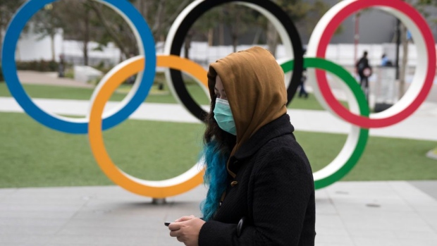 TOKYO, JAPAN - FEBRUARY 26: A woman wearing a face mask walks past the Olympic rings in front of the new National Stadium, the main stadium for the upcoming Tokyo 2020 Olympic and Paralympic Games, on February 26, 2020 in Tokyo, Japan. Concerns that the Tokyo Olympics may be postponed or cancelled are increasing as Japan confirms 862 cases of Coronavirus (COVID-19) and as some professional sporting contests are being called off or rescheduled and some major Japanese corporations ask for people to work from home. (Photo by Tomohiro Ohsumi/Getty Images)