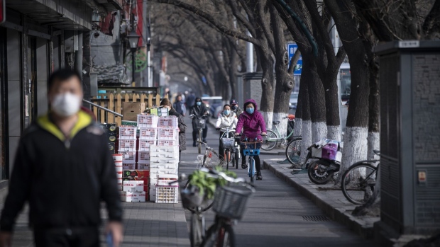 Commuters wearing protective masks ride bicycles down a street in Beijing on March 18. Photographer: Qilai Shen/Bloomberg