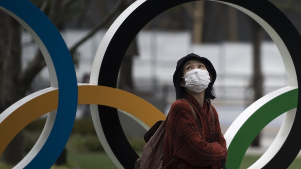 TOKYO, JAPAN - FEBRUARY 26: A woman wearing a face mask walks past the Olympic rings in front of the new National Stadium, the main stadium for the upcoming Tokyo 2020 Olympic and Paralympic Games, on February 26, 2020 in Tokyo, Japan. Concerns that the Tokyo Olympics may be postponed or cancelled are increasing as Japan confirms 862 cases of Coronavirus (COVID-19) and as some professional sporting contests are being called off or rescheduled and some major Japanese corporations ask for people to work from home. (Photo by Tomohiro Ohsumi/Getty Images)