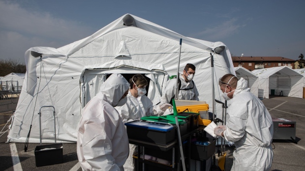 Workers, wearing protective suits, stand in front of a tent at an emergency field hospital in Cremona, Italy, on March 20. Photographer: Emanuele Cremaschi/Getty Images