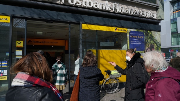 BERLIN, GERMANY - MARCH 18: People, including one woman wearing a protective face mask against the coronavirus, wait to enter a branch of bank Postbank on March 18 in Berlin, Germany. Everyday life in Germany has become fundamentally altered as authorities tighten measures to stem the spread of the coronavirus. Public venues such as bars, clubs, museums, cinemas, schools, daycare centers and non-essential shops have closed. Many businesses are resorting to home office work for their employees. And travel across the border to most neighboring countries is severely restricted. (Photo by Sean Gallup/Getty Images)