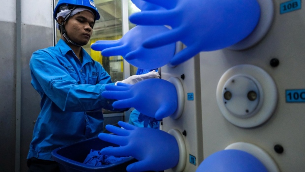 Employees attach latex gloves to an air compressor as other gloves are inflated in the air-leak test room at a Top Glove Corp. factory in Setia Alam, Selangor, Malaysia, on Tuesday, Feb. 18, 2020. The world’s biggest glovemaker got a vote of confidence from investors in the credit market, as the coronavirus fuels demand for the Malaysian company’s rubber products. The World Health Organization is taking an unprecedented step of negotiating directly with suppliers to improve access to gloves, face masks and other forms of protective equipment. Photographer: Samsul Said/Bloomberg
