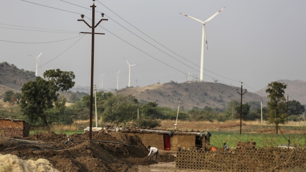 Laborers work below an electricity pole operated by Maharashtra State Electricity Distribution Co. (MSEDCL) as Suzlon Energy Ltd. wind turbines stand in the background in Nadurbar district, Maharashtra, India, on Tuesday, Jan. 17, 2017. Indian Prime Minister Narendra Modi pledged to bring reliable power to all citizens during the campaign that propelled him into office in 2014, the same year the World Bank pegged India as home to the world's largest un-electrified population. While his government has made progress meeting its 2019 deadline, many families are still missing out, holding back some of India's poorest, most-vulnerable citizens and preventing the country from achieving its development ambitions. Photographer: Dhiraj Singh/Bloomberg