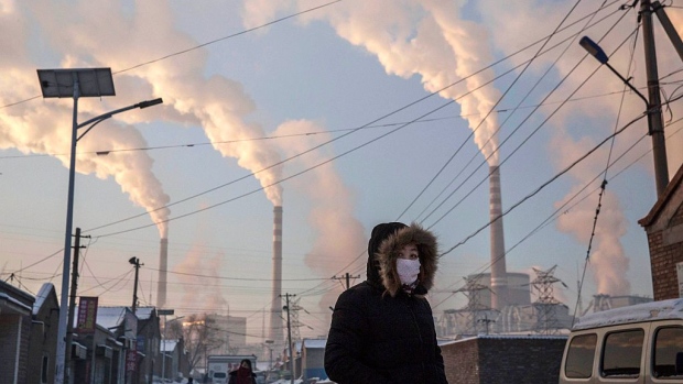 SHANXI, CHINA -NOVEMBER 26: (CHINA, HONG KONG, MACAU, TAIWAN OUT) Smoke billows from stacks as a Chinese woman wears as mask while walking in a neighborhood next to a coal fired power plant on November 26, 2015 in Shanxi, China. A history of heavy dependence on burning coal for energy has made China the source of nearly a third of the world's total carbon dioxide (CO2) emissions, the toxic pollutants widely cited by scientists and environmentalists as the primary cause of global warming. China's government has publicly set 2030 as a deadline to reach the country's emissions peak, and data suggest the country's coal consumption is already in decline. The governments of more than 190 countries are expected to sign an agreement in Paris to set targets on reducing carbon emissions in an attempt to forge a new global agreement on climate change. (Photo by Kevin Frayer/Getty Images) Photographer: Kevin Frayer/Getty Images AsiaPac