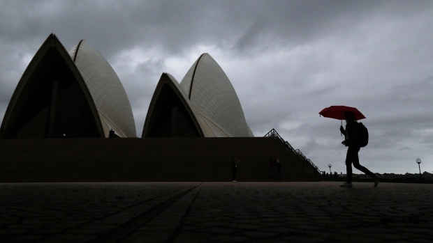 A pedestrian holding an umbrella walks past the closed Sydney Opera House stands in Sydney, Australia, on Tuesday, March 24, 2020. Australia's parliament rushed through more than A$80 billion ($46.3 billion) in fiscal stimulus for the coronavirus-stricken economy at a special sitting in Canberra on March 23. Photographer: Brendon Thorne/Bloomberg