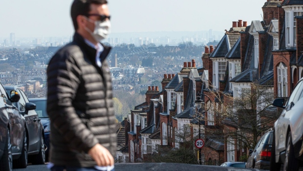 A pedestrian wearing a protective face mask walks past residential properties in London, U.K., on Friday, March 27, 2020. U.K. house sales are set to plunge by 60% in the next three months as the coronavirus outbreak batters the economy. Photographer: Hollie Adams/Bloomberg