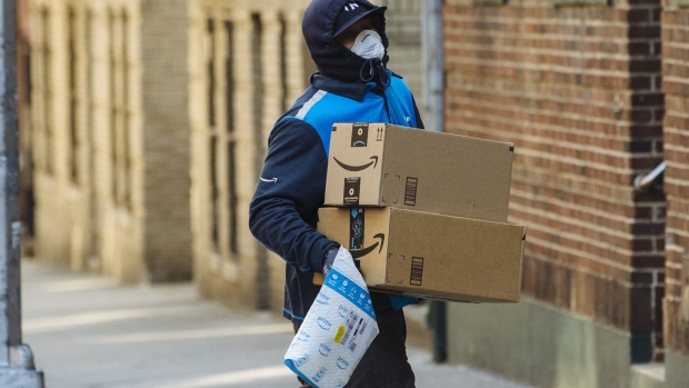 A worker wearing a protective mask and gloves carries Amazon.com Inc. boxes during a delivery in the Bronx borough of New York, U.S., on Thursday, March 26, 2020. New York City is the epicenter of the coronavirus pandemic in the United States, putting historic pressure on a world-renowned healthcare system as the number of confirmed cases in the area grows exponentially. Photographer: Angus Mordant/Bloomberg