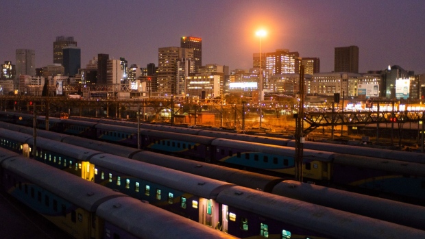 Commercial office buildings stand illuminated on the city skyline beyond trains at the Johannesburg Park railway station in the central business district of Johannesburg, South Africa, on Tuesday, Aug. 8, 2019. Eskom Holdings SOC Ltd., South Africa’s biggest polluter, said emissions of particulate matter that cause chronic respiratory disease are at their highest level in two decades as the state power utility’s financial meltdown has seen it skip maintenance and has triggered strikes. Photographer: Waldo Swiegers/Bloomberg