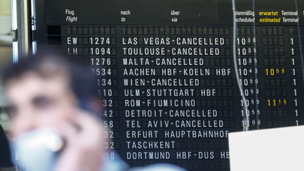 A traveler wears face masks near a flight departure information board showing cancelled flights to Las Vegas and Detroit at Frankfurt Airport, on March 12. Photographer: Alex Kraus/Bloomberg