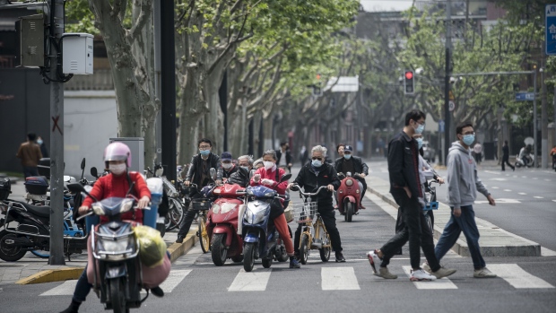 Pedestrians wearing protective masks walk across a road past motorists waiting at a traffic signal light in Shanghai, China, on Monday, April 20, 2020. 