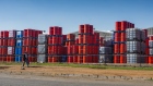 A pedestrian wearing a protective face mask walks by oil barrels stacked beyond security fencing at a facility in the Alrode district of Johannesburg, South Africa, on Tuesday, April 21, 2020. 
