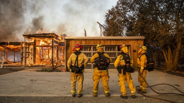 Firefighters survey a home burning along Highway 128 during during the Kincade fire in Healdsburg, California, U.S., on Sunday, Oct. 27, 2019. The wildfire that erupted in California’s wine country minutes after a PG&E Corp. power line went down has prompted an expanded evacuation order, as officials warn high winds could drive the blaze toward one of the region’s largest towns. Photographer: Phil Pacheco/Bloomberg