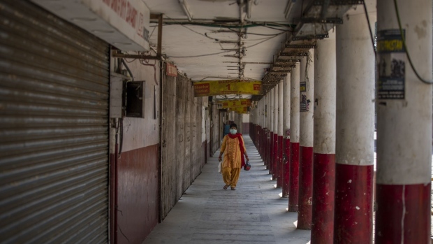 A pedestrian wearing a protective mask walks past shuttered stores in a near-empty Connaught Place during a partial lockdown imposed due to the coronavirus in New Delhi, India, on Thursday, May 14, 2020. India spelled out the details of its massive rescue package that will initially help small businesses and utility companies as Prime Minister Narendra Modi gears to restart the economy cratered by the coronavirus pandemic. Photographer: Prashanth Vishwanathan/Bloomberg