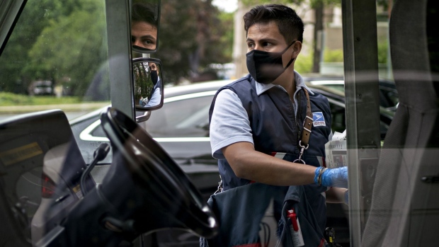 A United States Postal Service (USPS) letter carrier wears a protective mask and gloves while closing the door of a vehicle in Fairfax, Virginia, U.S., on Tuesday, May 19, 2020. The Postal Service in recent weeks has sought bids from consulting firms to reassess what the agency charges companies such as Amazon, UPS and FedEx to deliver products on their behalf between a post office and a customer's home, the Washington Post reported last week. Photographer: Andrew Harrer/Bloomberg