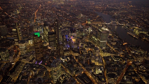 Lights illuminate the windows of skyscrapers and commercial office buildings as they stand alongside the banks of the River Thames in this aerial photograph looking east towards Canary Wharf and across the City of London, U.K. Photographer: Matthew Lloyd/Bloomberg