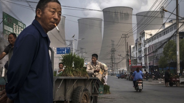 HUAINAN, CHINA - JUNE 14: Chinese street vendors sell vegetables at a local market outside a state owned Coal fired power plant near the site of a large floating solar farm project under construction by the Sungrow Power Supply Company on a lake caused by a collapsed and flooded coal mine on June 14, 2017 in Huainan, Anhui province, China. The floating solar field, billed as the largest in the world, is built on a part of the collapsed Panji No.1 coal mine that flooded over a decade ago due to over-mining, a common occurence in deep-well mining in China's coal heartland. When finished, the solar farm will be made up of more than 166,000 solar panels which convert sunlight to energy, and the site could potentially produce enough energy to power a city in Anhui province, regarded as one of the country's coal centers. Local officials say they are planning more projects like it, marking a significant shift in an area where long-term intensive coal mining has led to large areas of subsidence and environmental degradation. However, the energy transition has its challenges, primarily competitive pressure from the deeply-established coal industry that has at times led to delays in connecting solar projects to the state grid. China's government says it will spend over US $360 billion on clean energy projects by 2020 to help shift the country away from a dependence on fossil fuels, and earlier this year, Beijing canceled plans to build more than 100 coal-fired plants in a bid to ease overcapacity and limit carbon emissions. Already, China is the leading producer of solar energy, but it also remains the planet's top emitter of greenhouse gases and accounts for about half of the world's total coal consumption. (Photo by Kevin Frayer/Getty Images)