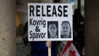 A young man holds a sign bearing photographs of Michael Kovrig and Michael Spavor