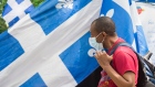 A man wears a face mask as he walks by a house adorned with Quebec flags on St-Jean Baptiste Day in 