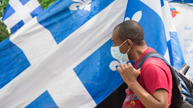 A man wears a face mask as he walks by a house adorned with Quebec flags on St-Jean Baptiste Day in 