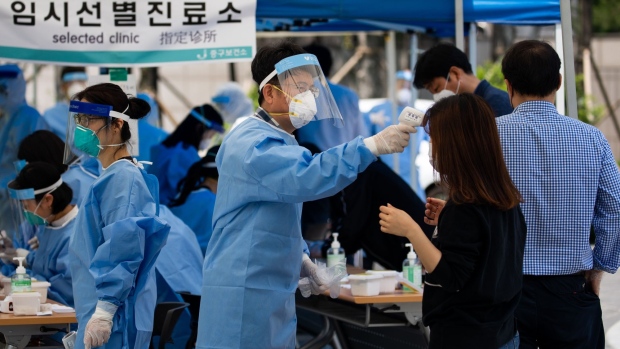 A medical worker in protective gear checks a temperature of a woman at a temporary coronavirus testing station in Seoul, South Korea, on Friday, May 29, 2020. In the wake of the new cluster, the South Korean government said it was temporarily closing public museums, parks and galleries in the Seoul metropolitan area and may consider stronger social distancing measures if the situation worsens.