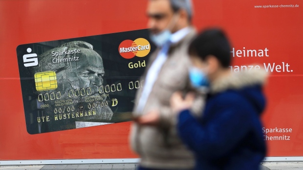 Pedestrians wearing protective face masks pass a Sparkassen Mastercard Inc. Gold credit card advertisement, featuring Karl Marx, in Chemnitz, Germany, on Thursday, April 30, 2020. In Germany, labor-market figures showed jobless claims rose by a record 373,000 in April, far exceeding all estimates in a Bloomberg survey.