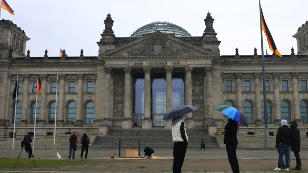 Pedestrians shelter under umbrellas outside the Bundestag building in Berlin, Germany, on Monday, May 4, 2020. Germany reported the lowest number of new coronavirus infections and deaths since at least March 30, as the country continues a gradual easing of curbs on public life and allows the economy to slowly restart. Photographer: Krisztian Bocsi/Bloomberg