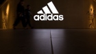 People walk past an illuminated Adidas sign. Photographer: SeongJoon Cho/Bloomberg