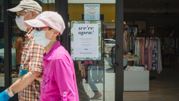 Pedestrians wearing protective masks pass in front of a sign that reads "We're Open!" outside a store in Fort Lauderdale, Florida, U.S., on Thursday, June 25, 2020. On Thursday, Florida reported more than 5,000 new confirmed cases of COVID-19 in the state, reported the Associated Press. Photographer: Jayme Gershen/Bloomberg