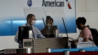 An American Airlines employee wears a protective mask and stands behind a protective barrier while checking in a traveler. Photographer: Andrew Harrer/Bloomberg