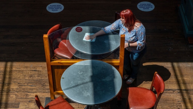 An employee cleans tables divided by a perspex screen at The Mossy Well pub, operated by J D Wetherspoons Plc, in this arranged photograph in London, U.K., on Wednesday, June 24, 2020. Hotels, pubs, restaurants and cinemas will be able to open their doors from July 4, U.K. Prime Minister said as he gave the green light for England's beleaguered tourism and hospitality industry to restart.