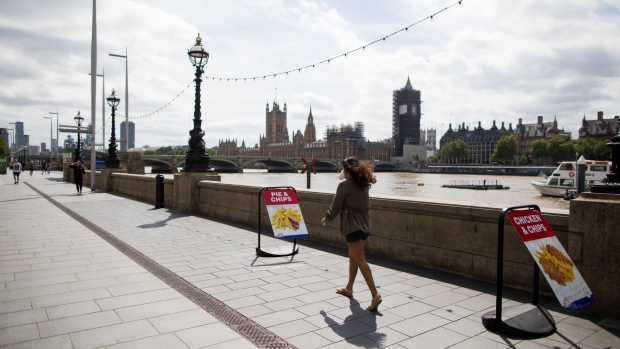 A pedestrian passes along the south bank of the River Thames against a backdrop of the Houses of Parliament in London, U.K., on Friday, July 3, 2020. As the U.K. prepares to reopen pubs, restaurants and hotels on July 4, the government and businesses are counting on the economy getting a big boost on the path to recovery. Photographer: Chris Ratcliffe/Bloomberg