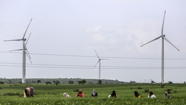 Workers tend the land as wind turbines manufactured by Inox Wind Ltd. operate beyond electricity cables at the Ostro Energy Pvt. Lahori Wind Farm in Lahori, Madhya Pradesh, India, on Monday, Aug. 14, 2017. As of June, India had 32 gigawatts of wind capacity. The nation is aiming to raise that to 60 gigawatts by 2022 as part of the country's climate pledge.