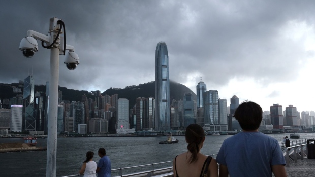 Pedestrians walk past a pair of security cameras along the Tsim Sha Tsui waterfront as buildings stand across Victoria Harbor in Hong Kong, China, on Tuesday, July 7, 2020. Hong Kong leader Carrie Lam defended national security legislation imposed on the city by China last week, hours after her government asserted broad new police powers, including warrant-less searches, online surveillance and property seizures.