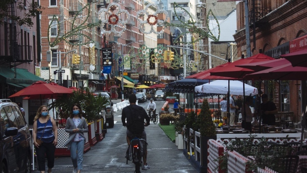 People wearing protective masks walk down a street lined with outdoor seating for restaurants in the Little Italy neighborhood of New York on July 6. Photographer: Angus Mordant/Bloomberg