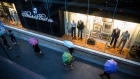 Pedestrians holding umbrellas walk past a Brooks Brothers store at the Gaysorn Village shopping mall in Bangkok. Photographer: Taylor Weidman/Bloomberg