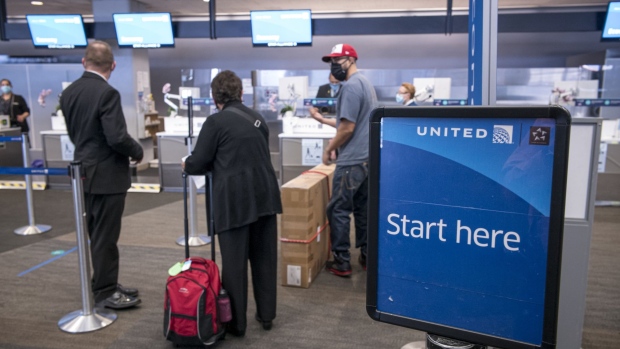 Travelers wearing protective masks get directions from an employee at a United Airlines Holdings Inc. counter at San Francisco International Airport (SFO) in San Francisco, California, U.S., on Wednesday, July 1, 2020. United Airlines Holdings Inc. plans to boost its domestic schedule for August to 48% of last years level, from 30% in July, offering another sign of rebounding travel demand.