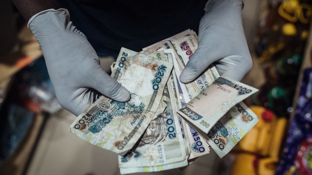 A vendor wearing protective latex gloves counts out Nigerian naira banknotes in a store in Lugbe district in Abuja, Nigeria, on Wednesday, June 3, 2020. The government of Nigeria, whose revenue could be slashed by more than half this year due to the oil-price slump, finalized plans for a revised budget that keeps spending almost intact, and that will mean more borrowing. Photographer: KC Nwakalor/Bloomberg